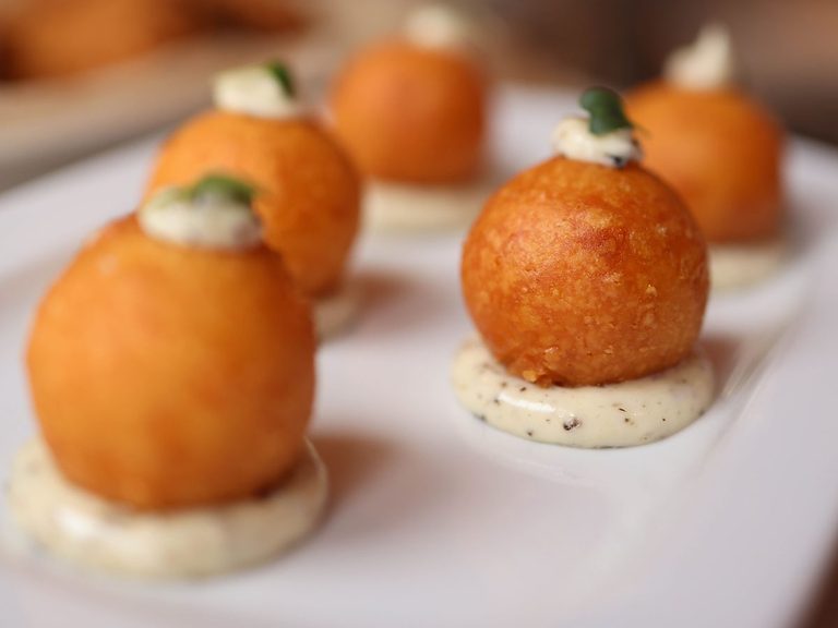 Golden crumbed arancini rice balls served on a white plate with aioli