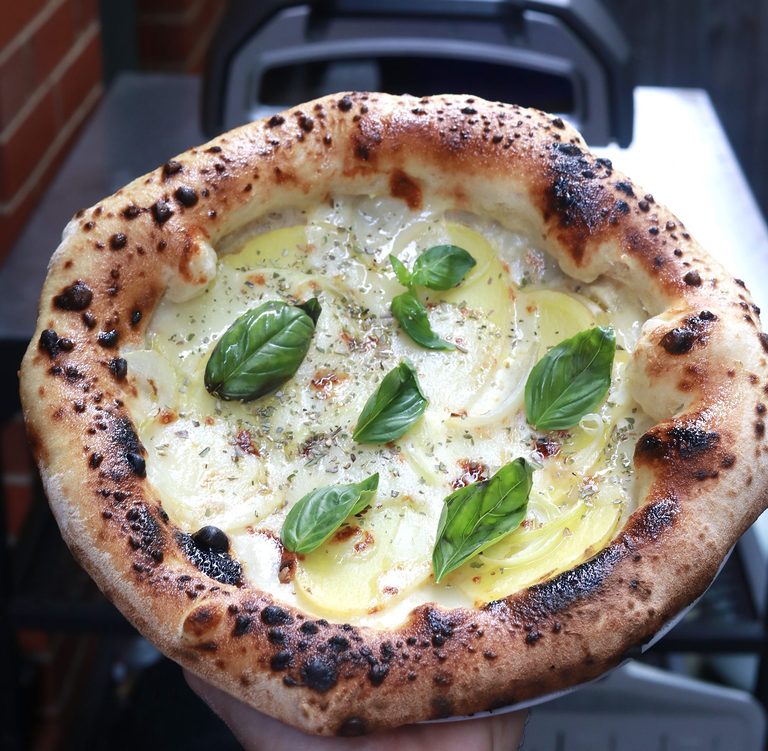 Potato and onion pizza with fresh basil, just out of a home pizza oven