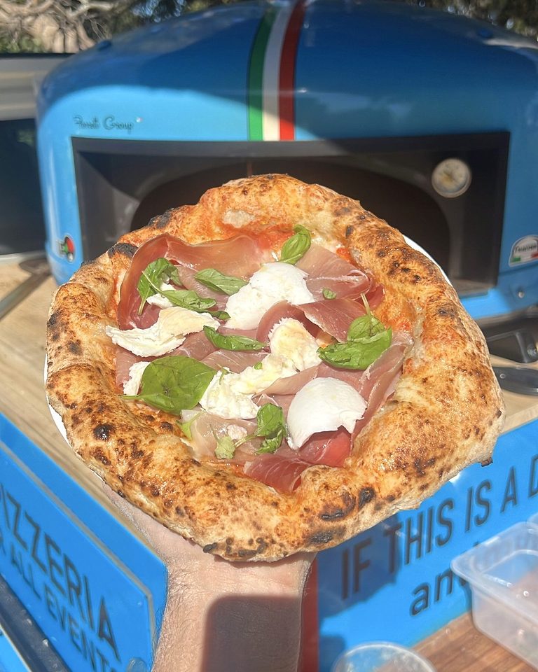 Wood-fired pizza with prosciutto, burrata and rocket in front of the blue oven, pizza catering Adelaide CBD