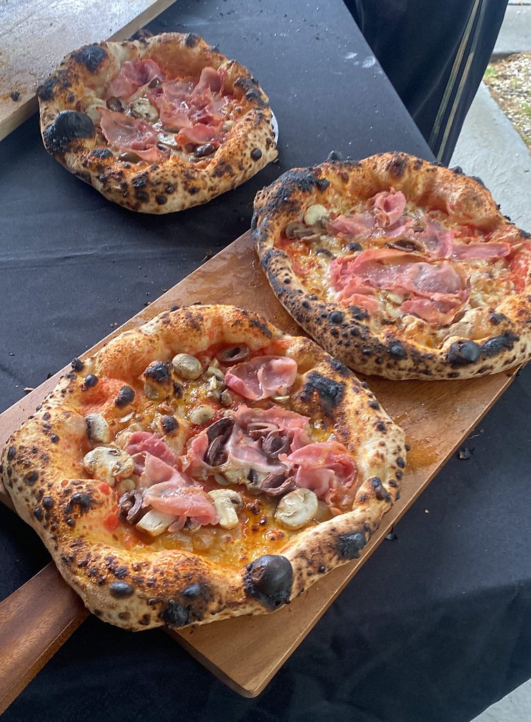 Three wood-fired pizzas with prosciutto, mushrooms and olives on a wooden board