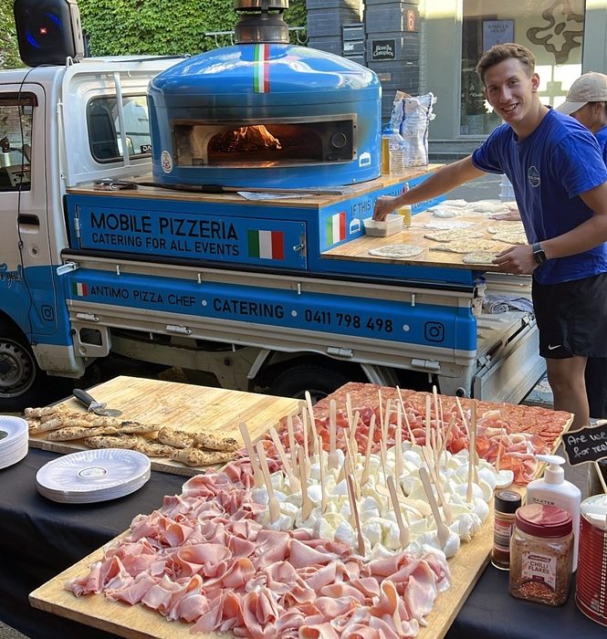 Antipasto boards of prosciutto, fresh mozzarella and salami in front of the blue Antimo Pizza Chef truck, with our team at the oven