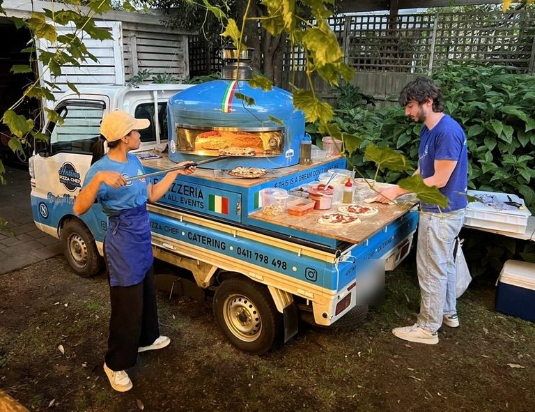 Our team cooking wood-fired pizzas at the blue pizza truck at a backyard party