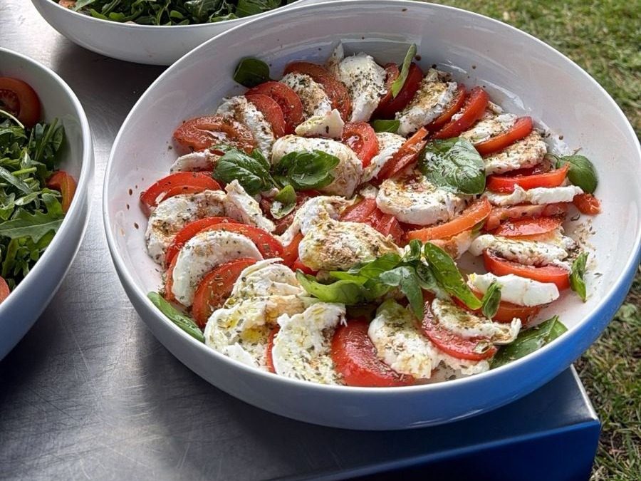 Caprese salad of tomato, mozzarella and basil in a white bowl beside a rocket salad