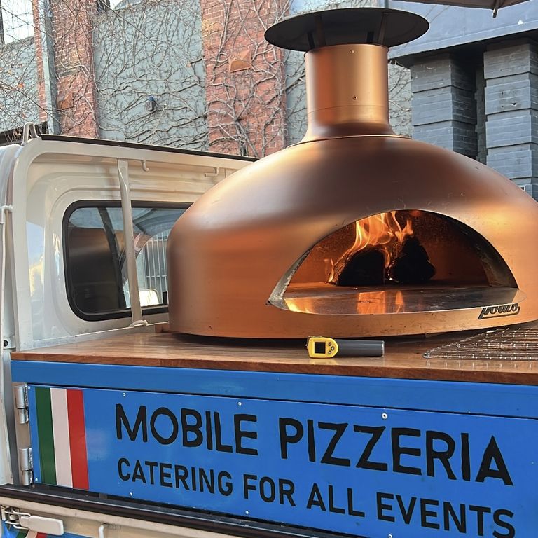 The copper wood-fired oven on our blue and white Adelaide pizza truck, fire lit and ready