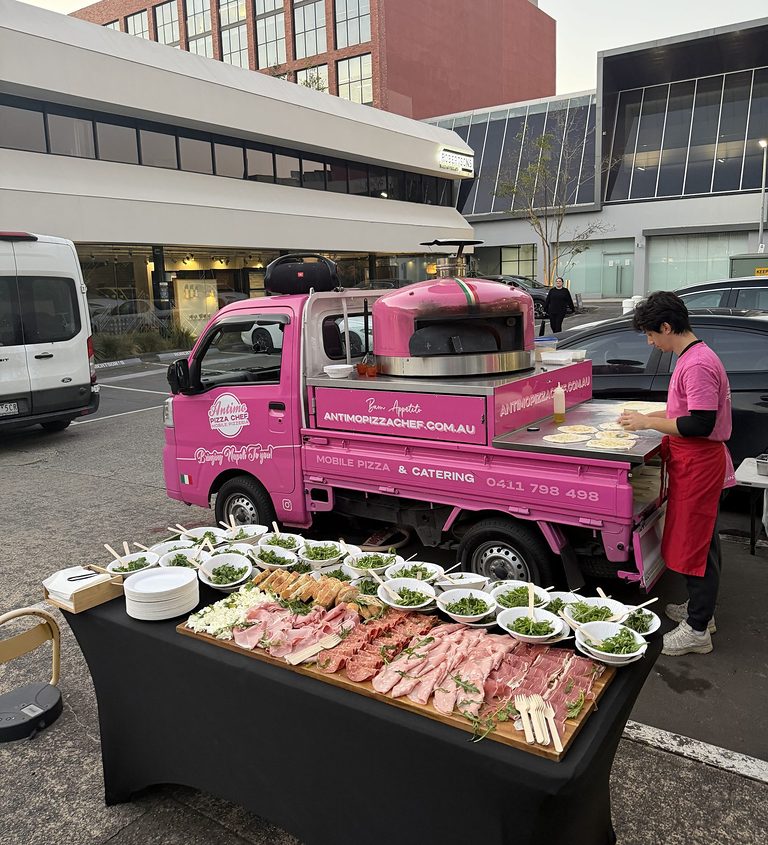 Corporate catering buffet with a wooden antipasto platter, individual rocket salad bowls and our chef prepping pizzas at the pink truck