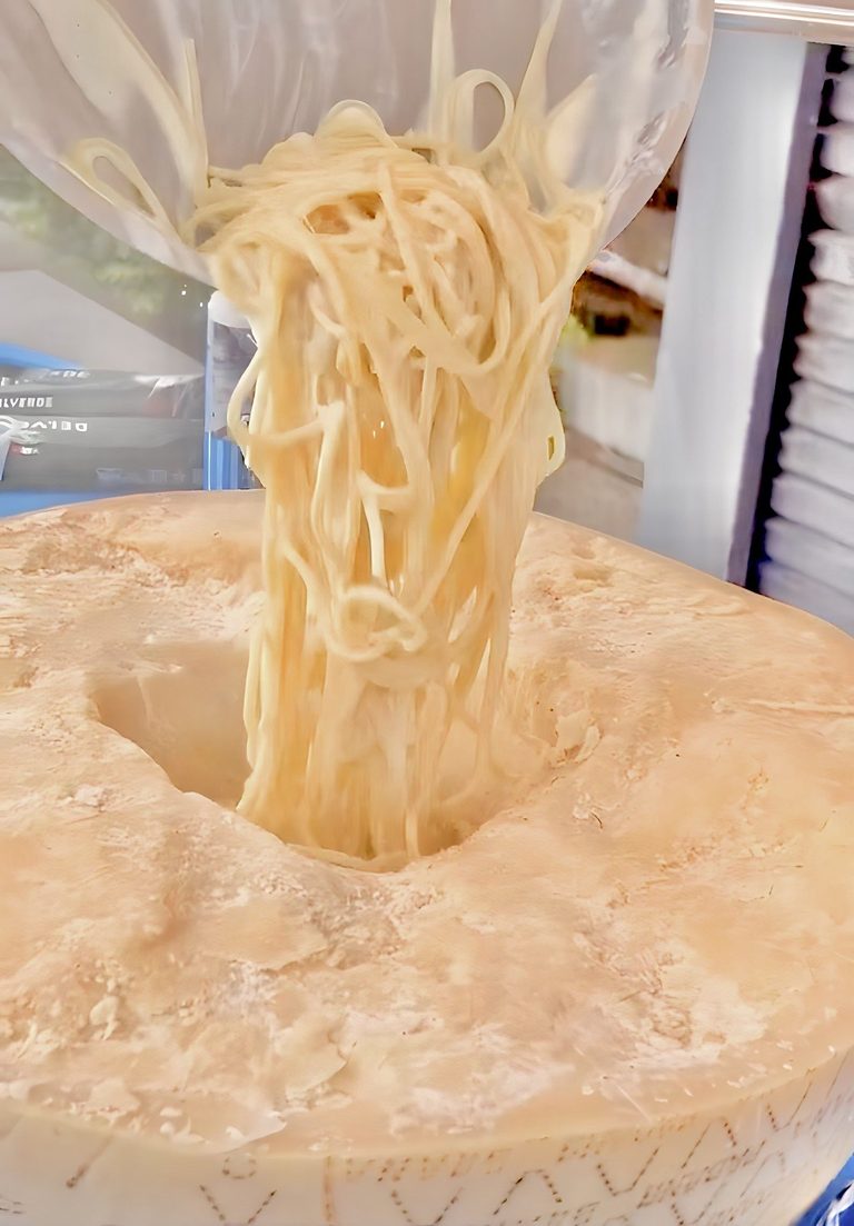 Fresh spaghetti lifted out of the cheese wheel with tongs