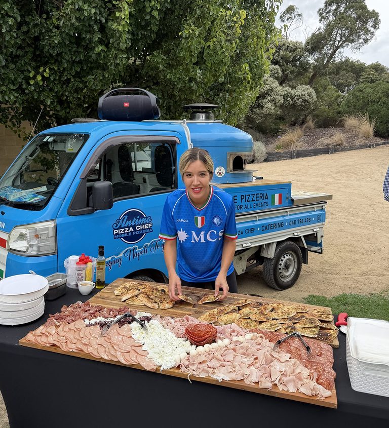 Our chef with a wooden antipasto and focaccia grazing platter in front of the blue Antimo Pizza Chef truck, pizza catering Penrith