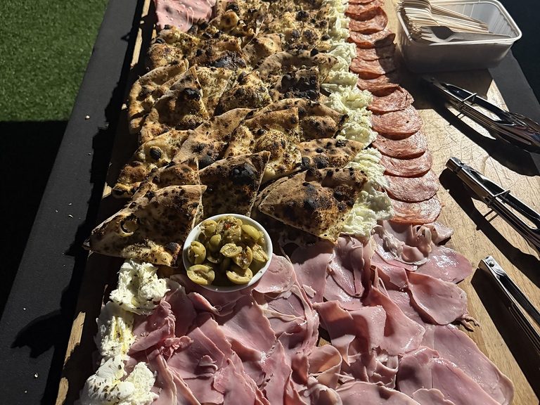Long wooden grazing plank with wood-fired garlic focaccia, green olives, fresh mozzarella, prosciutto and salami