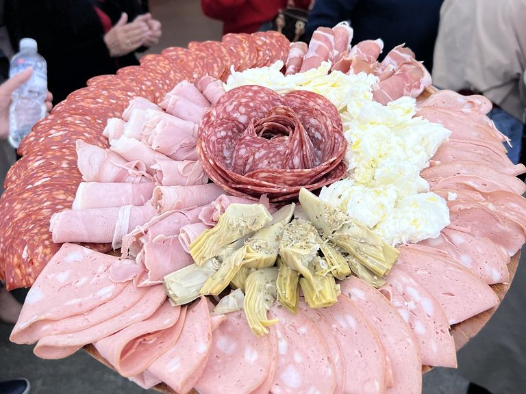 Round wooden antipasto board with a salami rosette, fresh mozzarella, mortadella, prosciutto and marinated artichokes
