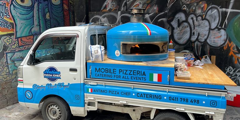 Pizza truck with a blue wood-fired oven by a street-art wall, pizza catering Sutherland Shire