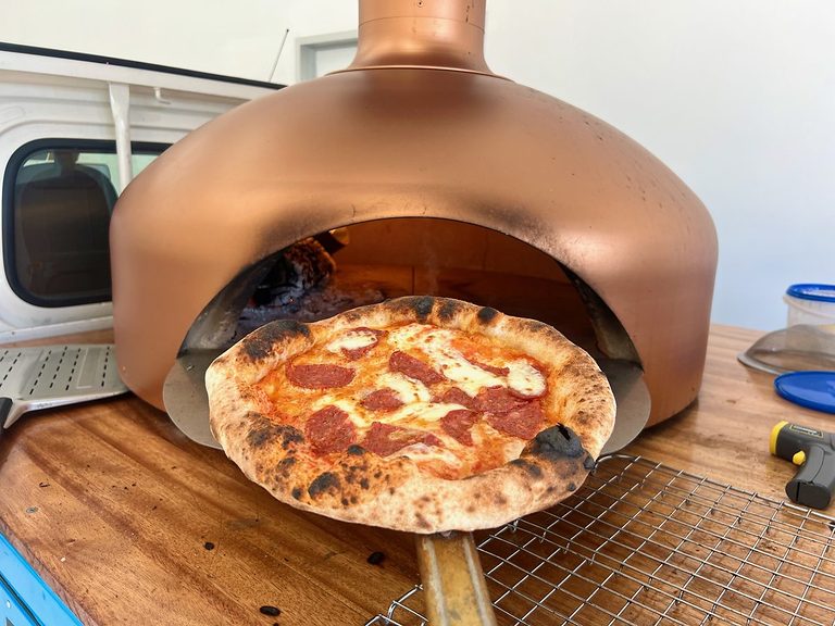 Wood-fired pepperoni pizza pulled on a wooden peel from the copper dome oven, pizza catering Adelaide CBD