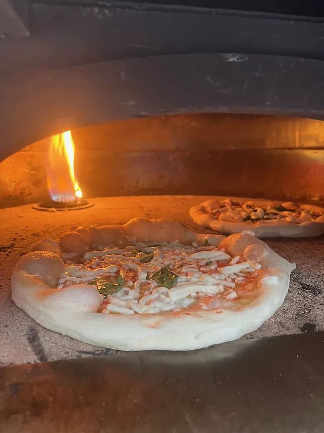 Two Neapolitan pizzas baking inside the wood-fired oven with live flames