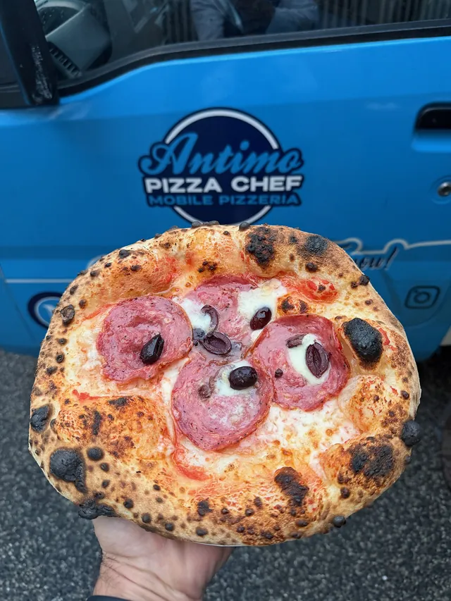 Wood-fired pepperoni and black olive pizza in front of the Antimo Pizza Chef truck