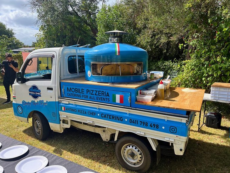 The blue and white Antimo Pizza Chef mobile pizzeria truck set up on a lawn