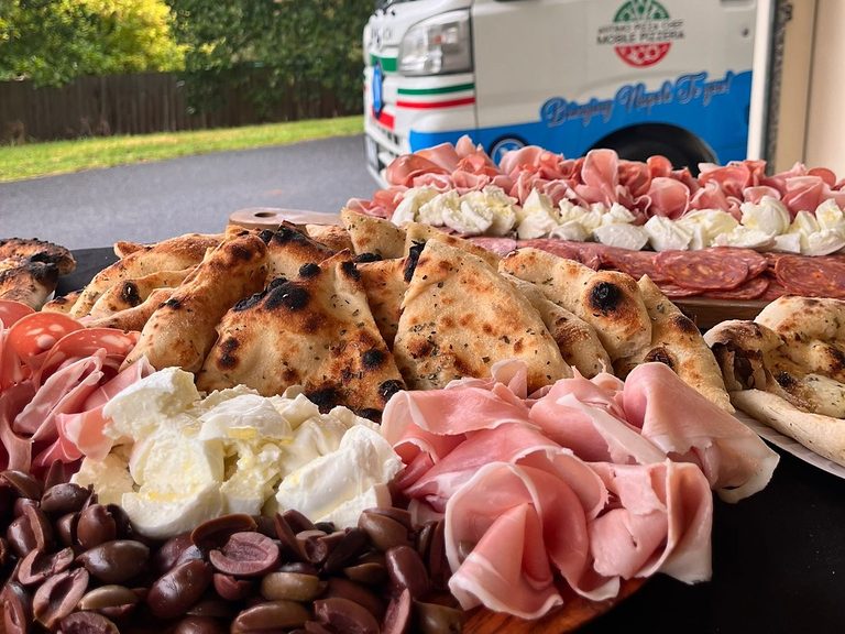 Antipasto platter with wood-fired garlic focaccia, buffalo mozzarella, prosciutto, salami and olives in front of the Antimo truck