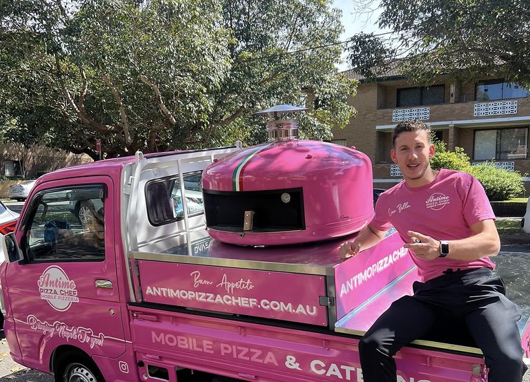 Matteo the Pizza Singer (@matteopizzasinger) sitting on the pink Antimo Pizza Chef mini truck with its wood-fired oven in Sydney