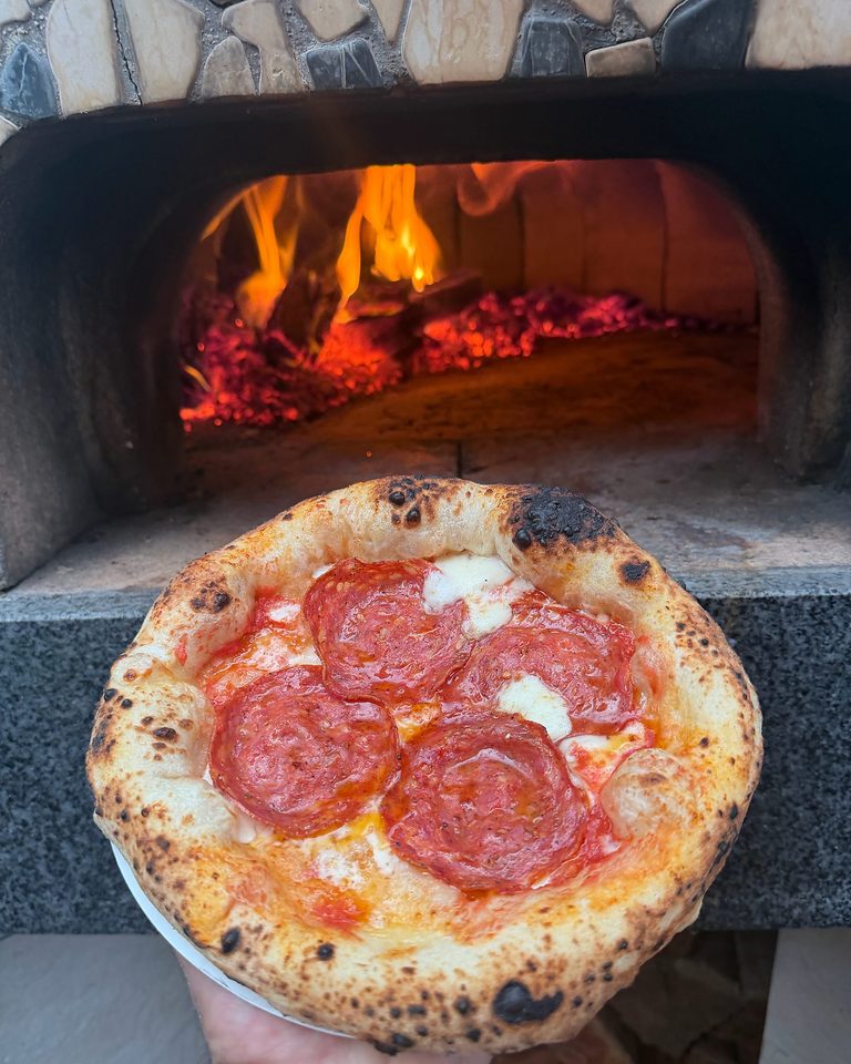 Wood-fired pepperoni pizza held up in front of a customer's own mosaic wood-fired oven (Own Oven set up, Melbourne)