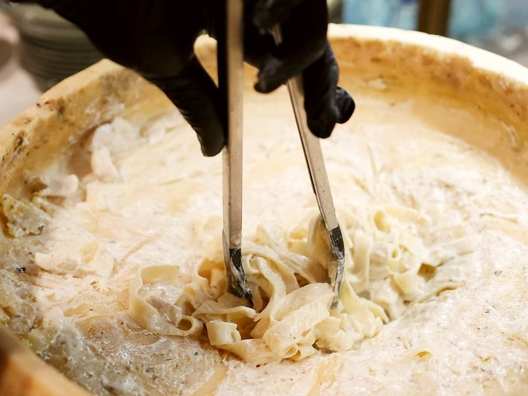Fresh pasta tossed live inside a 25 kg cheese wheel alongside wood-fired pizza catering in Melbourne