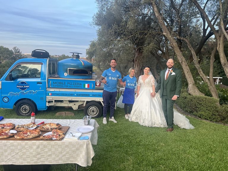 Bride and groom with Antimo and the blue mobile pizza truck at an outdoor wedding reception